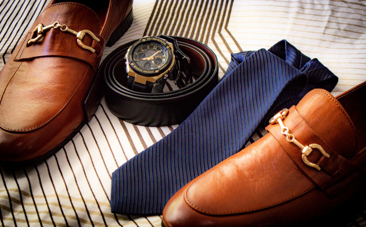 Close-up of elegant leather shoes, wristwatch, belt, and tie on striped fabric. Perfect for men's fashion.