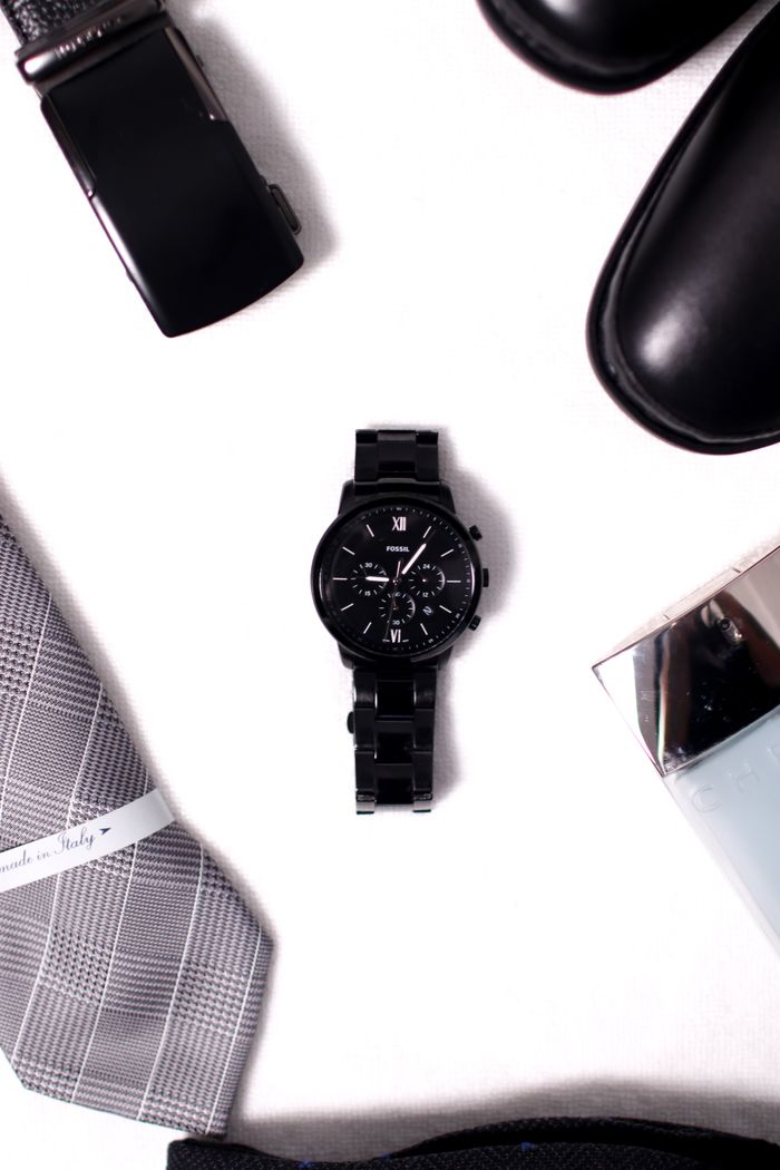 Stylish black wristwatch with men's fashion items on a white surface.